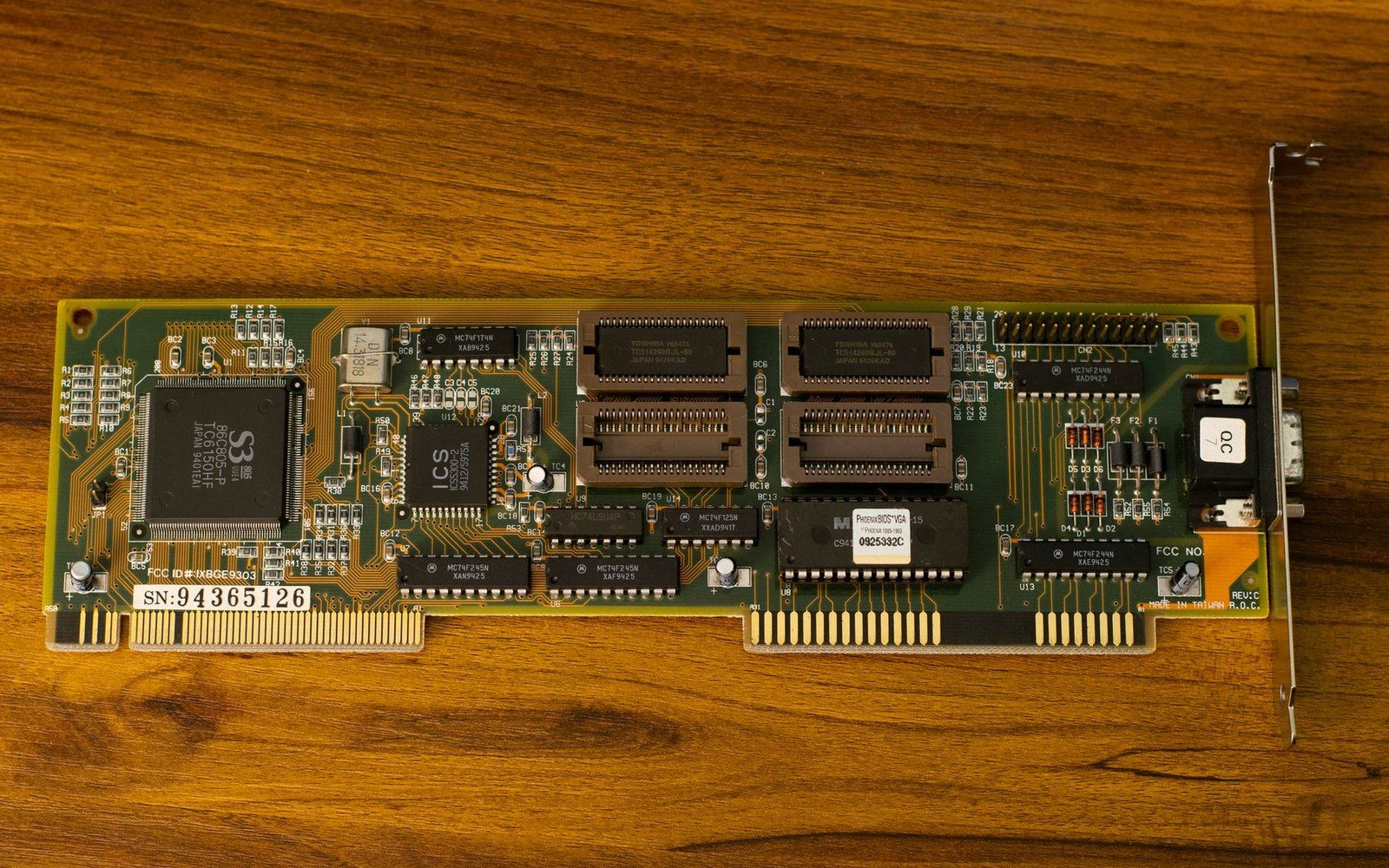 Green ISA expansion card with multiple chips and a metal mounting bracket on wood