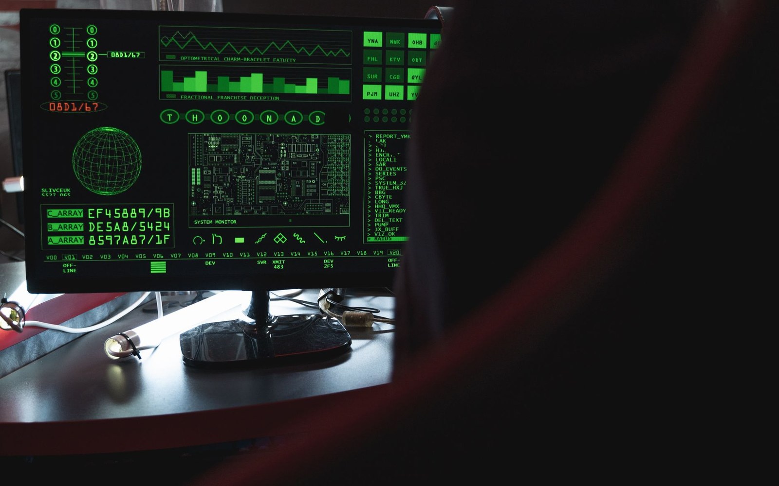 A computer monitor displays green retro-style data readouts and system graphics in a dark room